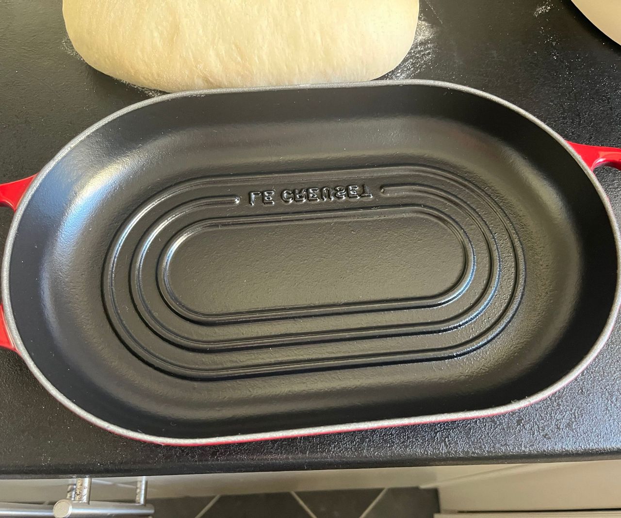 The base of a red Le Creuset oval bread oven on a black kitchen counter.