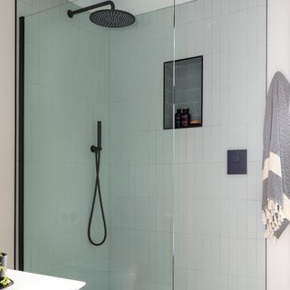 A close-up of a shower enclosure with matt black showerhead and accessories with nook containing bathing products in brown glass containers