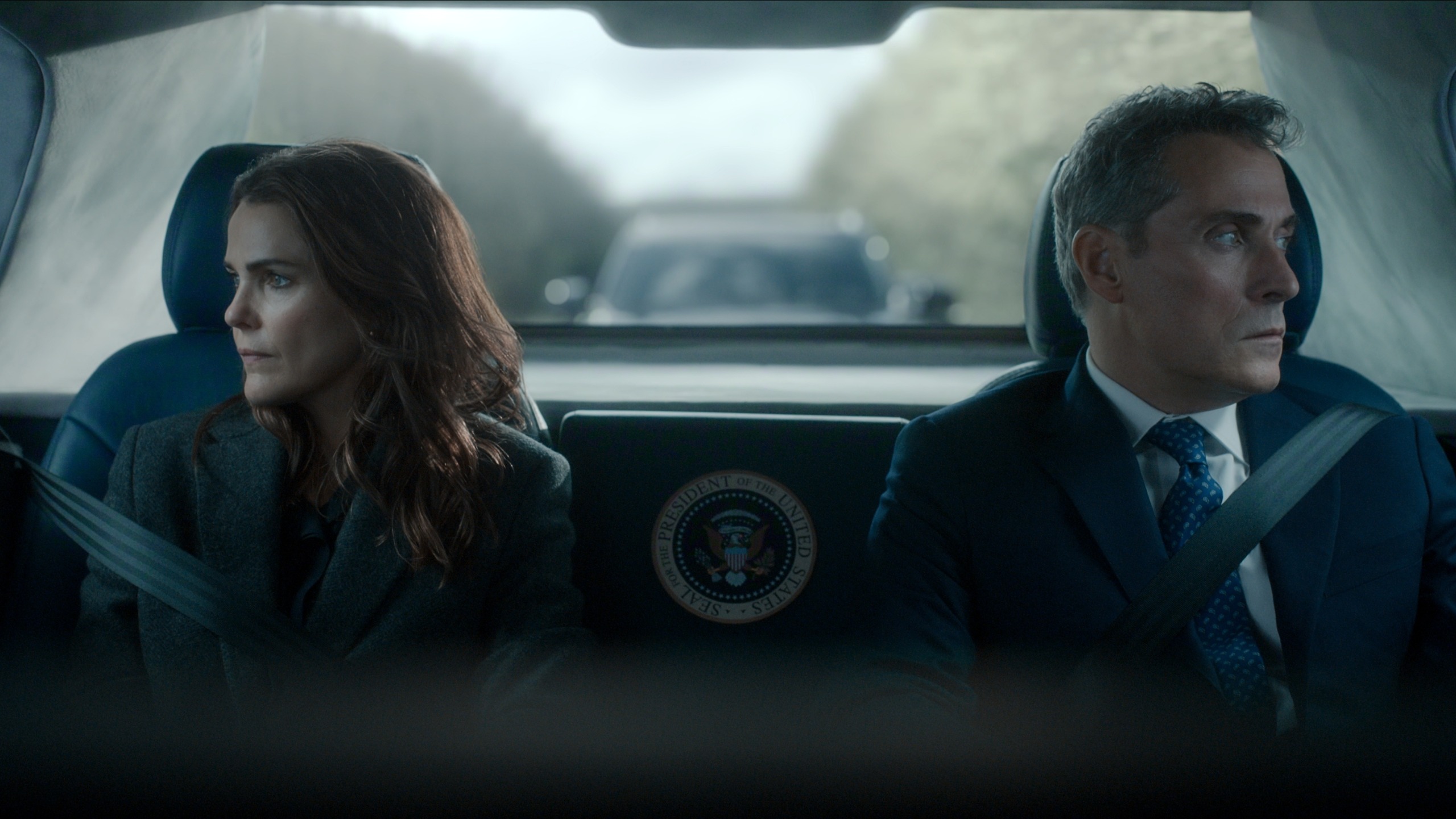 Keri Russell as Kate Wyler and Rufus Sewell as Hal Wyler sitting in a car looking away from each other and out of their windows.