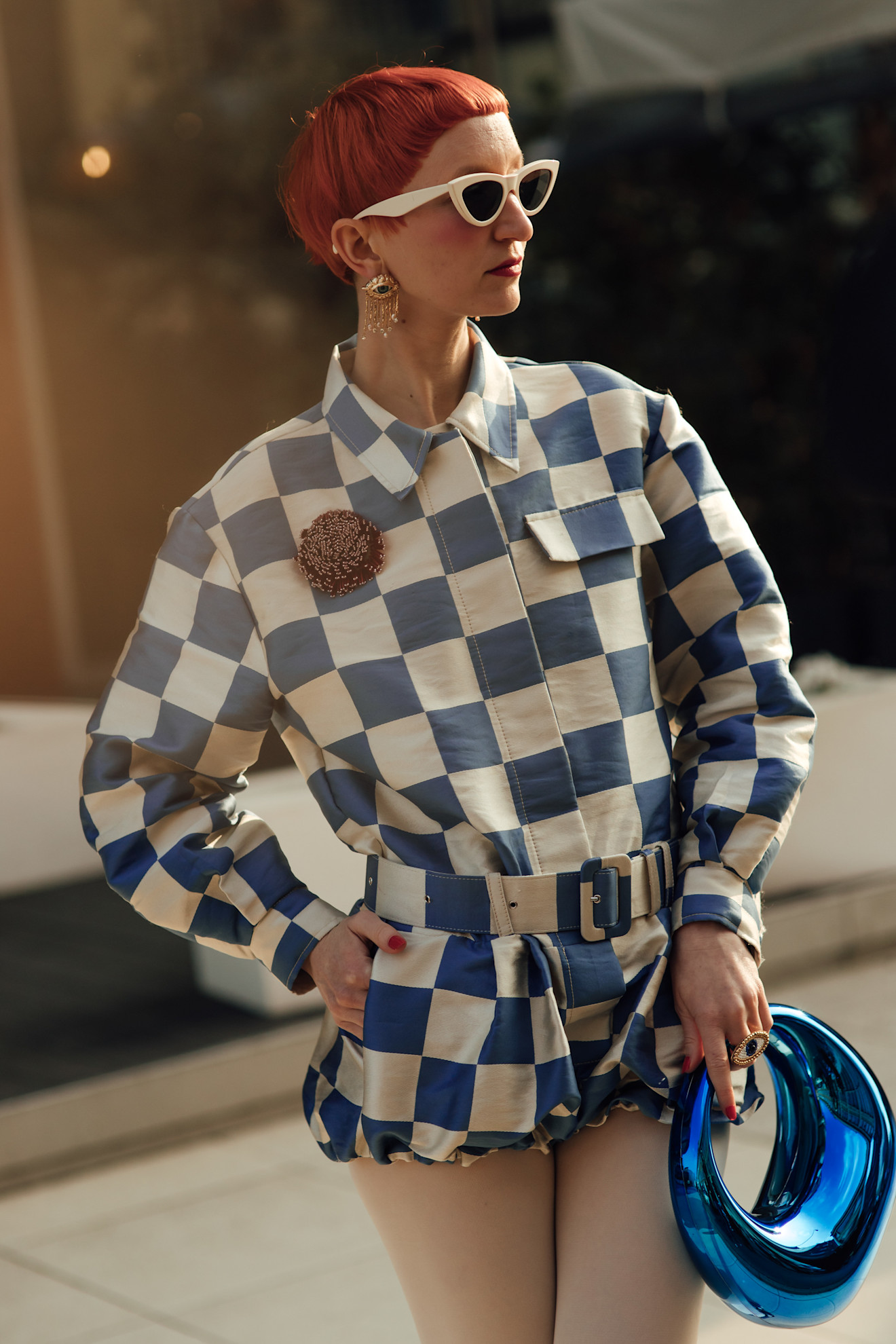 a woman with a red bowl cut and blue and white checkered jacket with a blue bag