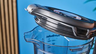 a black nutribullet with a big blending component is photographed in front of a blue backdrop, showing its plastic pitcher jug, silver blades, and tamper