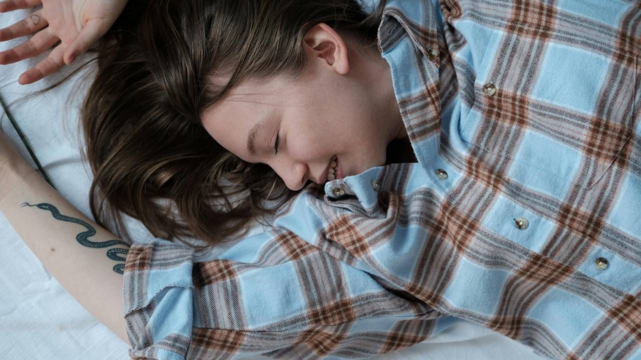 A woman in a checkered shirt, stretching on a bed and smiling while she sleeps