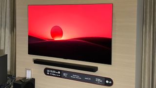 A wall-mounted LG G5 OLED TV displaying a red-tinted sunset