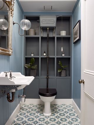 A blue powder room with traditional sanitaryware, mosaic floor tiles and gray open shelving