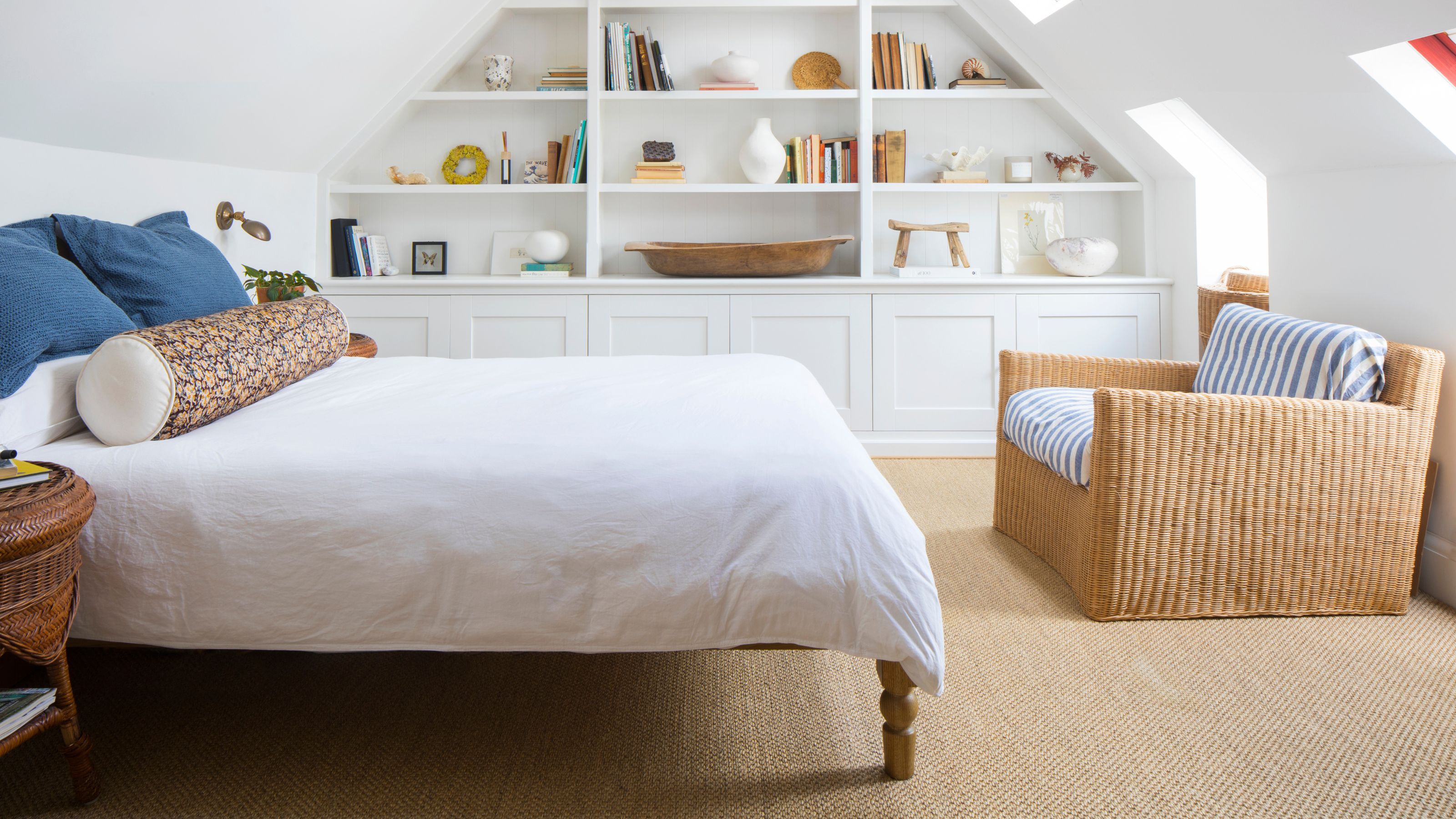 White painted loft bedroom with wool carpets, a bed with white bedding and a bookcase on the back wall