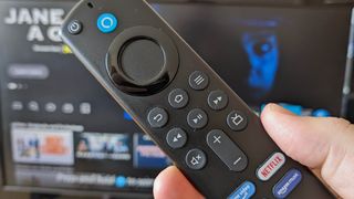 The Fire TV Stick 4K remote held in front of a TV displaying Fire OS.