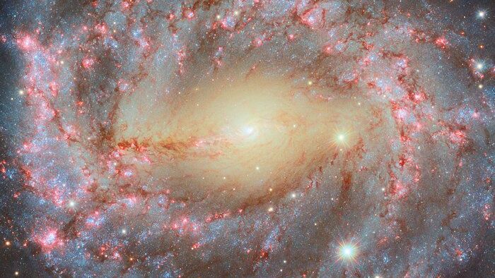 a giant swirling galaxy like an eye in space with a yellow center and red and white spiral arms.