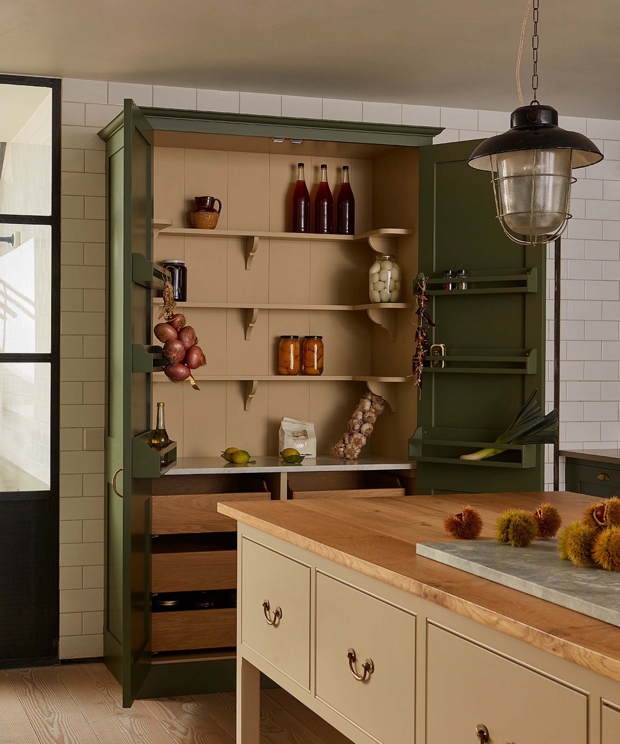 A country kitchen with a beige freestanding island and a forest green larder