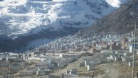 Image of La Rinconada showing lots of shelters on the side of a mountain. Another snow-covered mountain can be seen in the background.