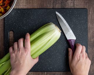 Woman’s hands, bunch of celery washed and ready to chop on a black cutting board with chef knife