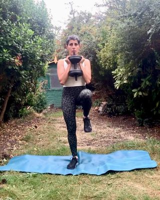 yanar alkayat woman short hair wearing white top dark leggings outside in garden holding weight doing weighted march