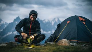 Hiker prepares hot beverage with headlamp in alpine campsite