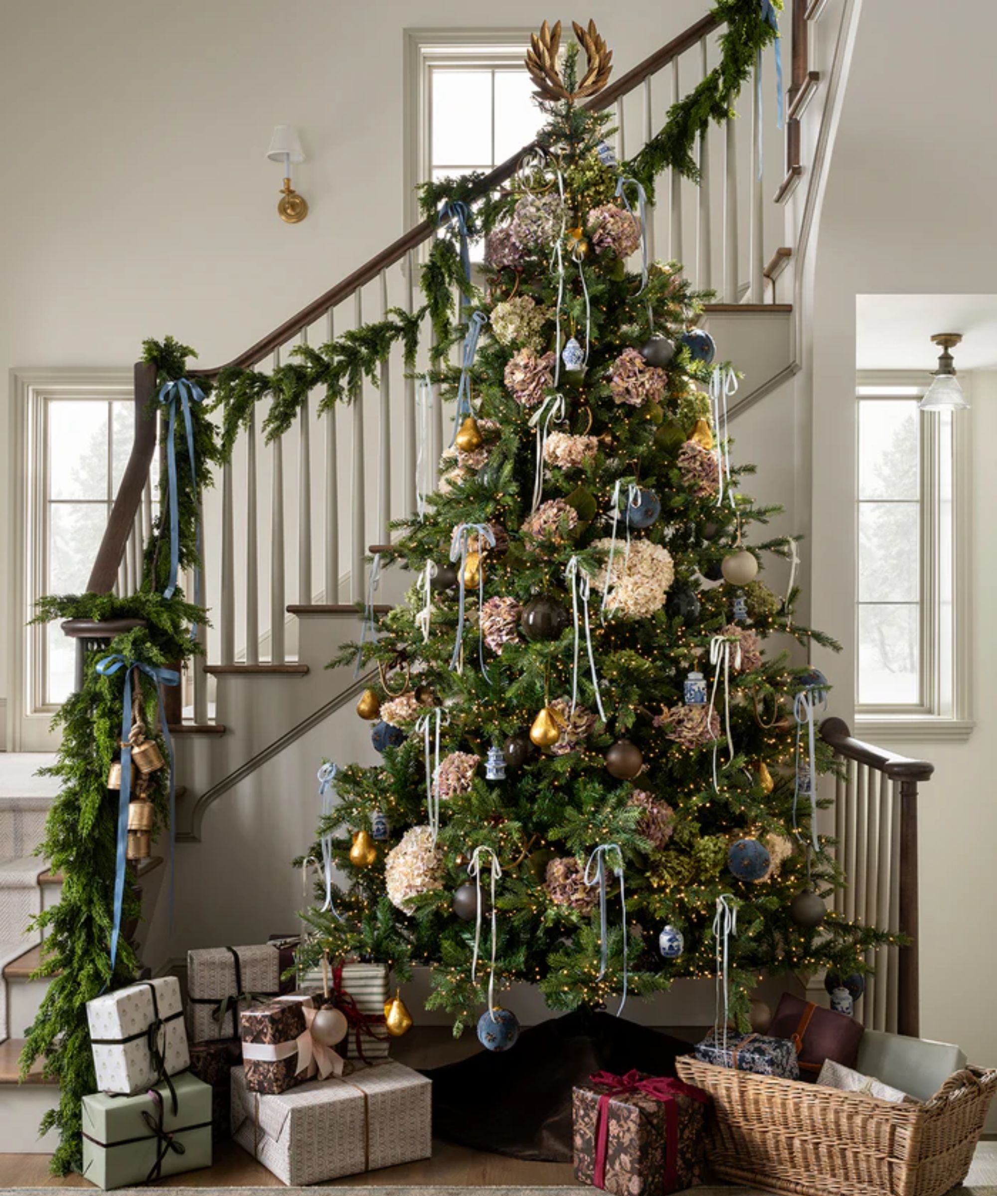mcgee and co christmas 2025 styled staircase with a foliage garland, ribbons and bells with a large decorated christmas tree and wrapped presents