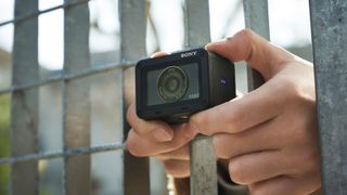 Sony RX0 II review: a person holds the camera through the bars of a steel fence to film