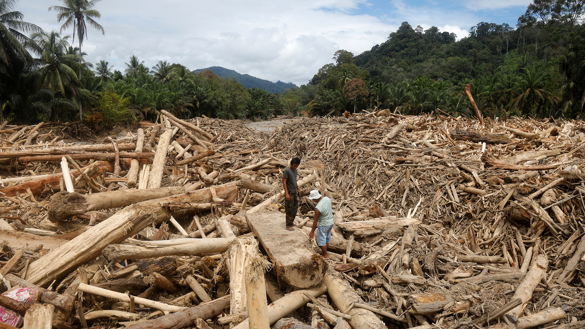 Men stand on debris swept away by a flash flood in Batang Toru, North Sumatra, Indonesia