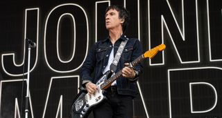 Johnny Marr plays a Fender Jaguar with lipstick pickups onstage, with his name in bold behind him.