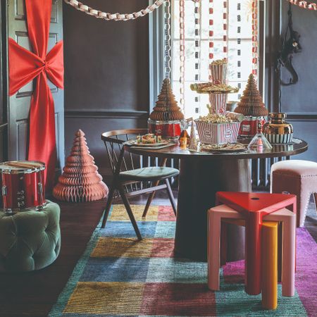 A dining room with a round table decorated for Christmas with stools and ottomans used for extra seating, as well as colourful stacked stools