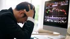 An investor puts his head in his hands in front of a trading graph on his computer.