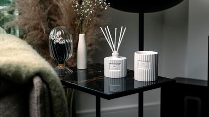 A white fluted candle jar and reed diffuser on a black glass side table. 