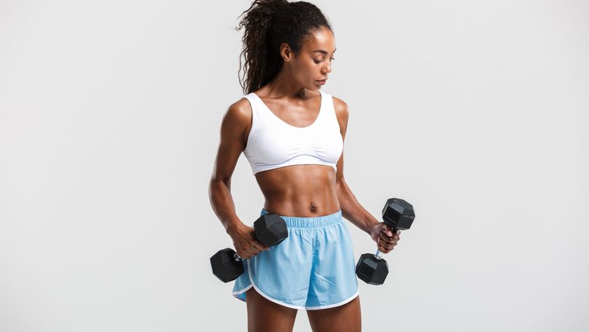 Woman against a grey backdrop in workout clothes holding two dumbbells in front of her during dumbbell workout