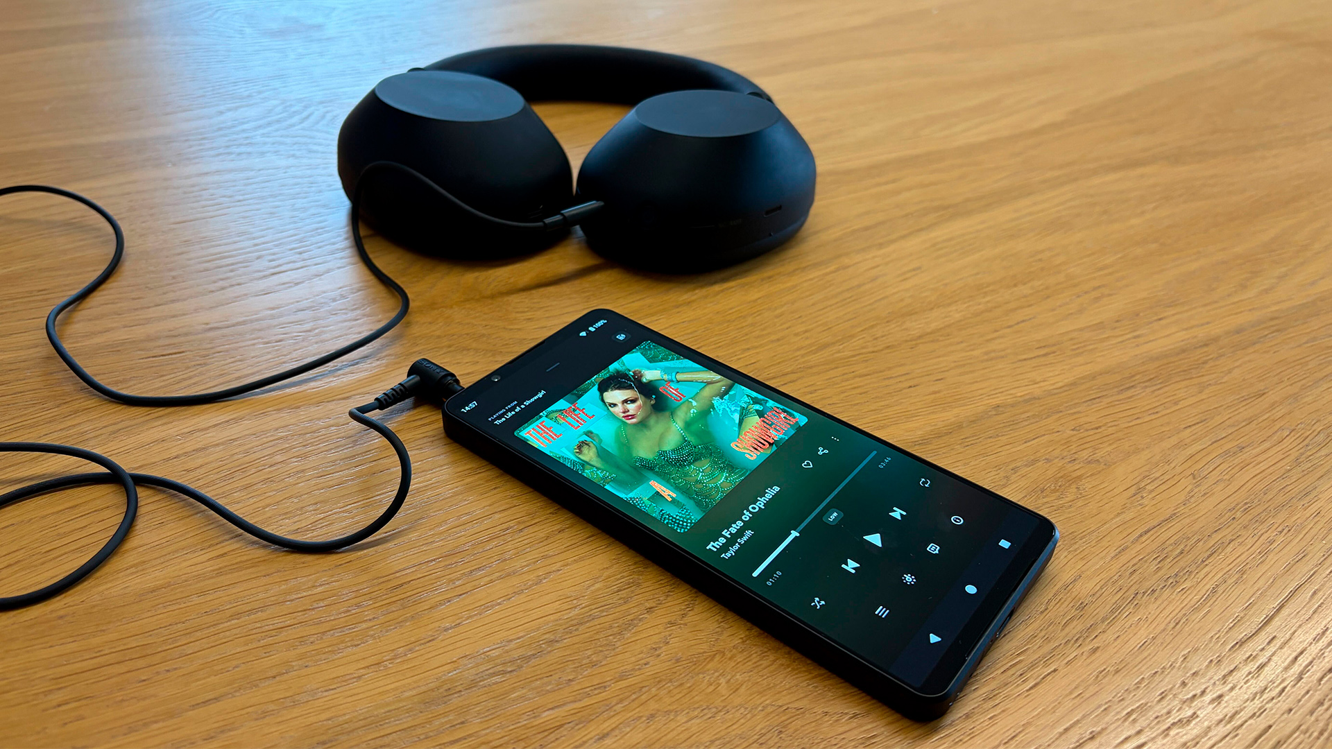 Sony Xperia 1 VII smartphone on wooden table with over-ear wired headphones plugged in