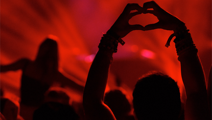 Person in audience with hands shaping a heart in red lighting