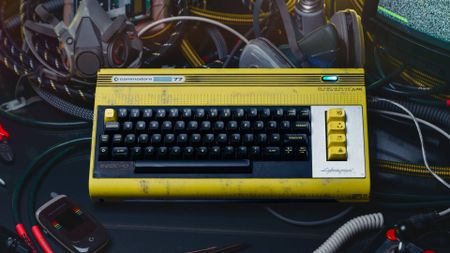 Commodore 77 version of C64 Ultimate on black desk next to Callback Flipphone and TAC joystick surrounded by wires and a CRT on the right hand side.