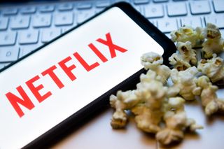 In this photo illustration a Netflix logo seen displayed on a smartphone with popcorns and laptop keyboard in the background.