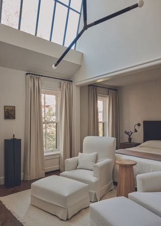 The primary suite bedroom, featuring tall ceilings with large windows and neutral soft furnishing