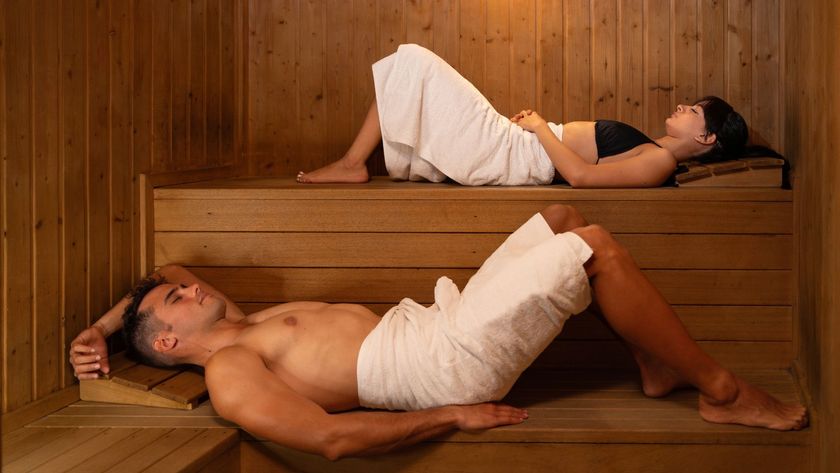A man and woman laying down in a wooden sauna with white towels wrapped around their waists