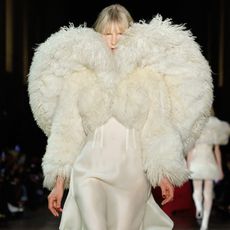 A model wearing a shearling and silk cream-colored coat and dress walking at the F/W 25 Alexander McQueen show.