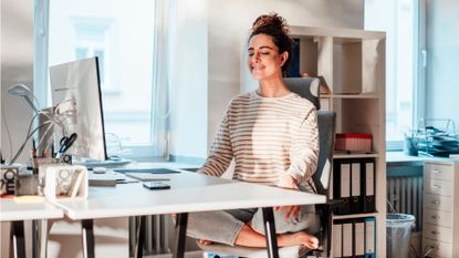 Woman sitting behind a desk, holding abdominal clenching pose to represent desk exercises to do at home or the office 