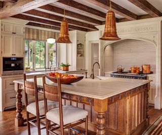 kitchen with island with turned legs range cooker with copper pans and white countertops and ceiling beams