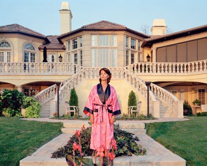 ‘Suburbia. Building the American Dream’ exhibition photo: woman in pink robe in front of grand suburban house