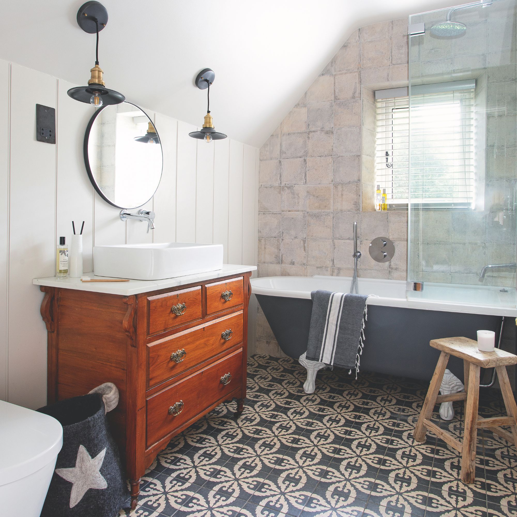 White bathroom with various different tiles on the wall and the floor, and a wooden vanity next to a blue shower bath