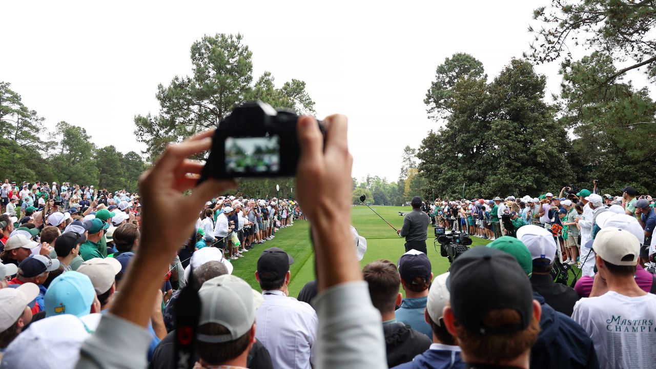 A camera lens seen as Tiger Woods plays a drive at The Masters