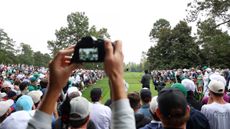 A camera lens seen as Tiger Woods plays a drive at The Masters