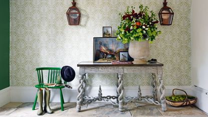 Entry table decor ideas with grey table, green wallpaper, flowers and paintings of pheasants
