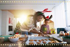 Woman and child cooking gingerbread biscuits together wearing reindeer antlers