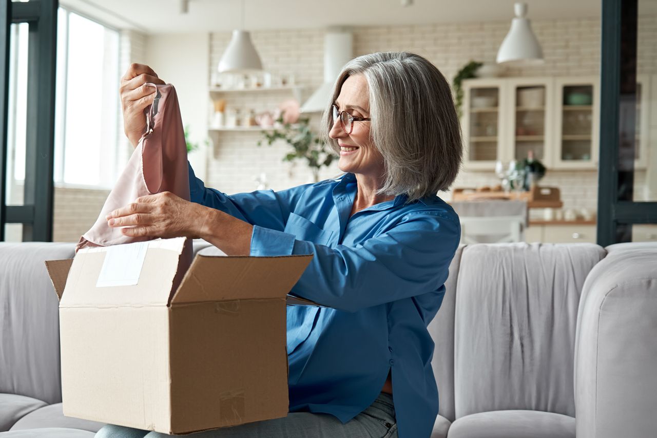 Smiling female customer unpacking clothing delivery on couch. 