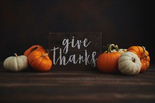 A pumpkin arrangement with orange and white pumpkins surrounding a sign that says give thanks.