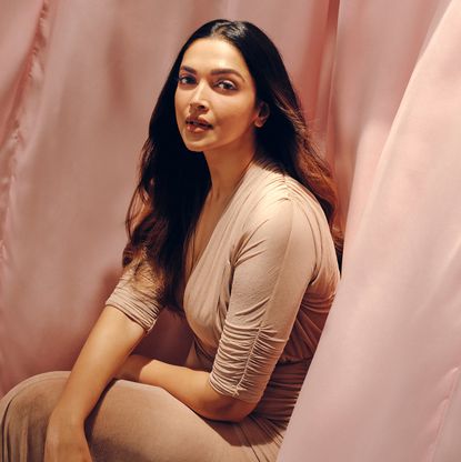 actress deepika padukone wearing a brown dress and posing as she's surrounded by blowing pink fabric