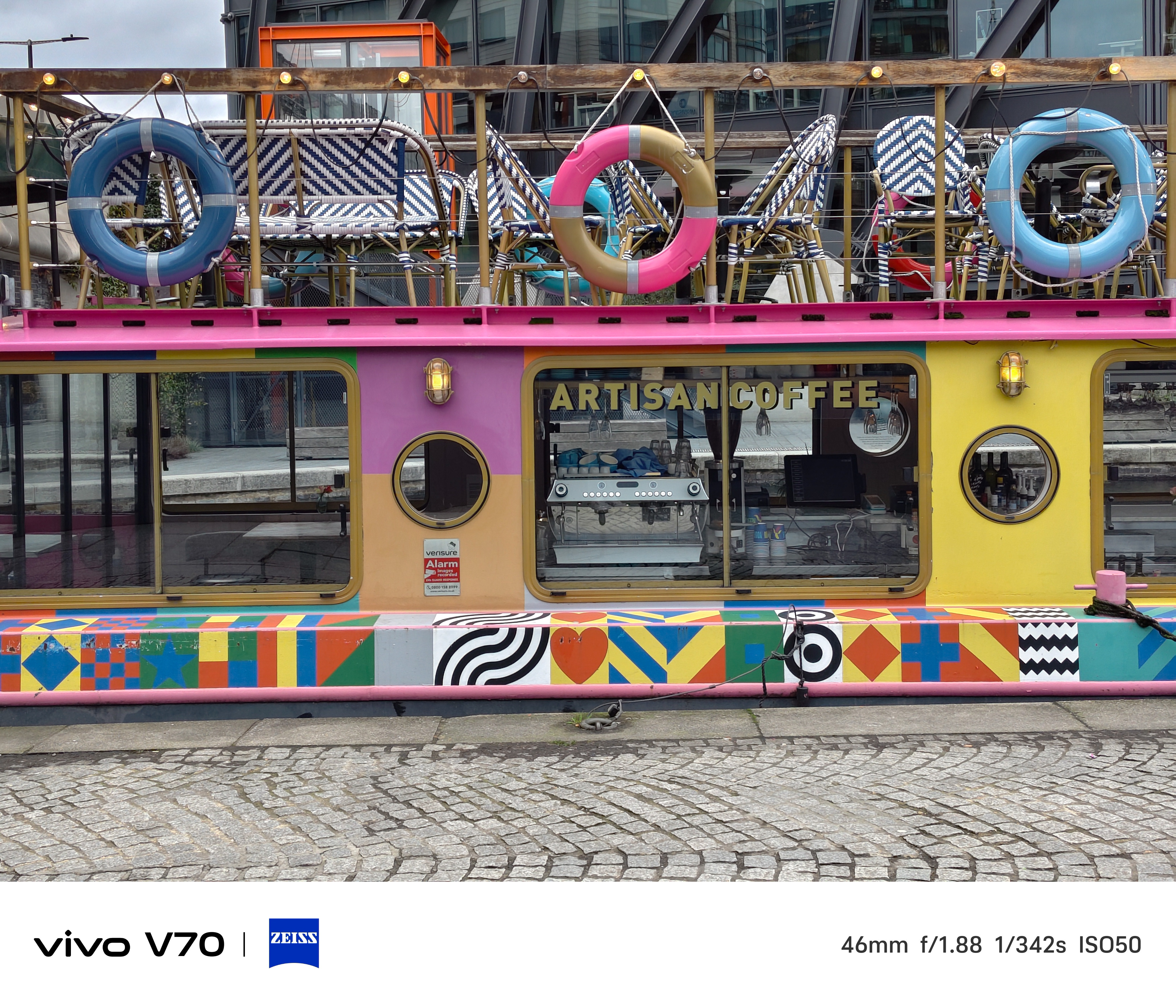 Colorful canal boat café with lifebuoys and “ARTISAN COFFEE” sign on side.