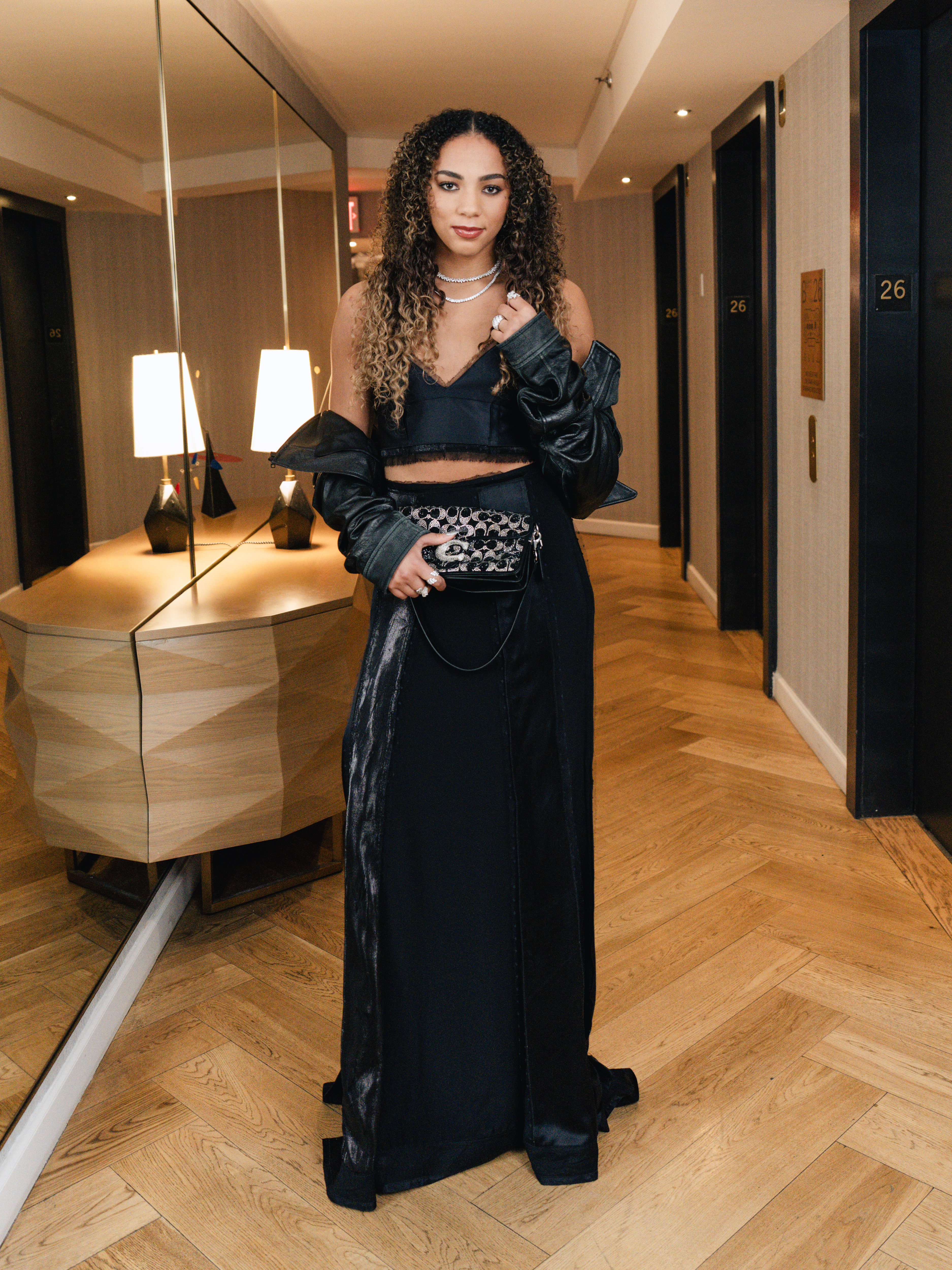 Kiki Rice wearing a custom Coach two-piece set with a leather jacket, platform heels, and a small shoulder bag for the WNBA Draft.