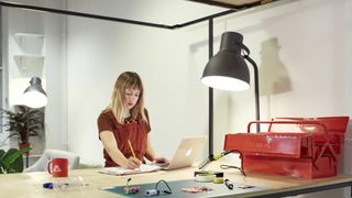 Woman writes in notebook on a wooden desk next to a laptop and large red toolbox