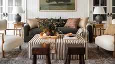 Shoppe Amber Interiors living room with shiplapped walls, a large dark sofa with a striped ottoman, two boucle armchairs and mini side tables