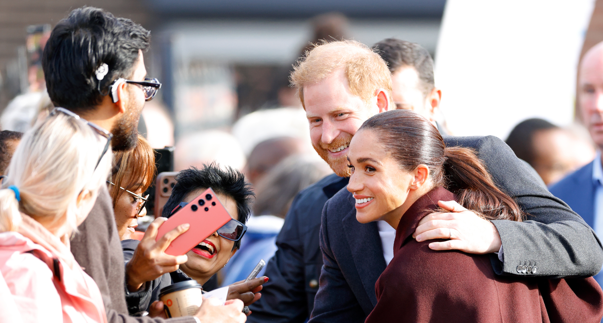 Prince Harry meeting fans with his arm around Meghan