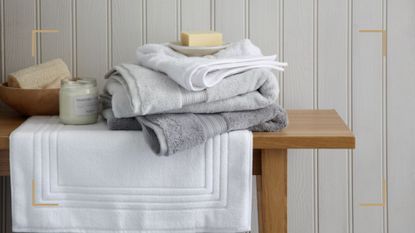 Wooden bench in bathroom with a stack of bathroom towels to support expert tips for how to soften towels for optimum fluffiness