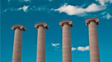 Four columns against a blue sky with clouds.