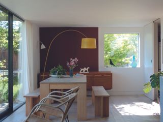 A dining room with a wooden dining bench, a curved floor lamp, and a deep red accent wall